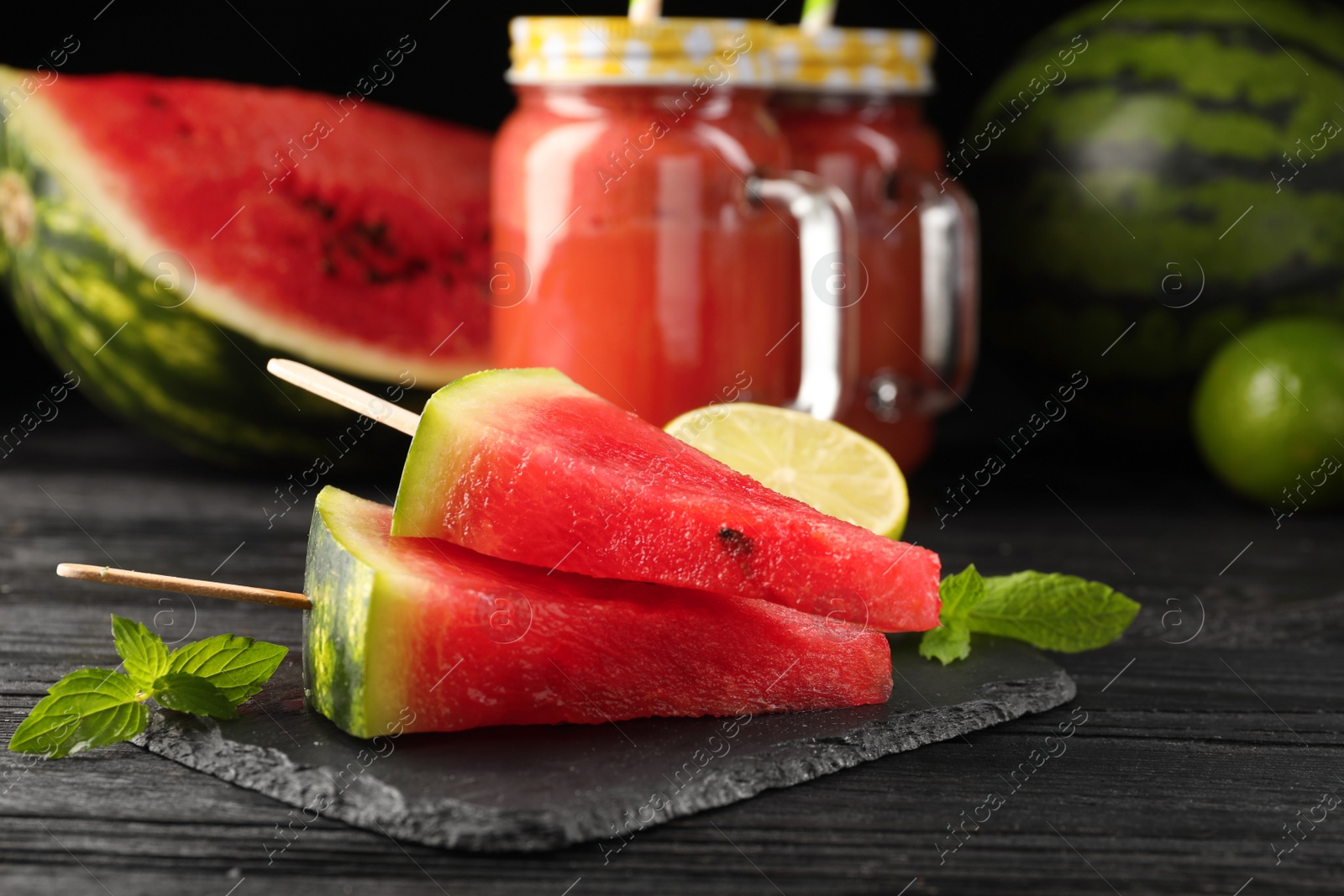 Photo of Slate board with cut juicy watermelon and lime on black wooden table
