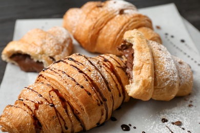 Photo of Tasty croissants with sugar powder and chocolate sauce, closeup