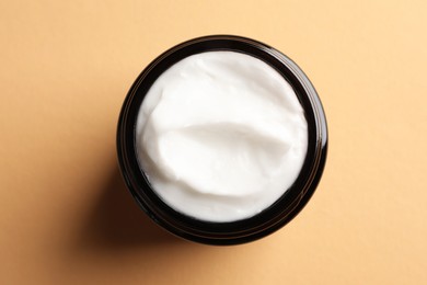 Jar of face cream on light orange background, top view