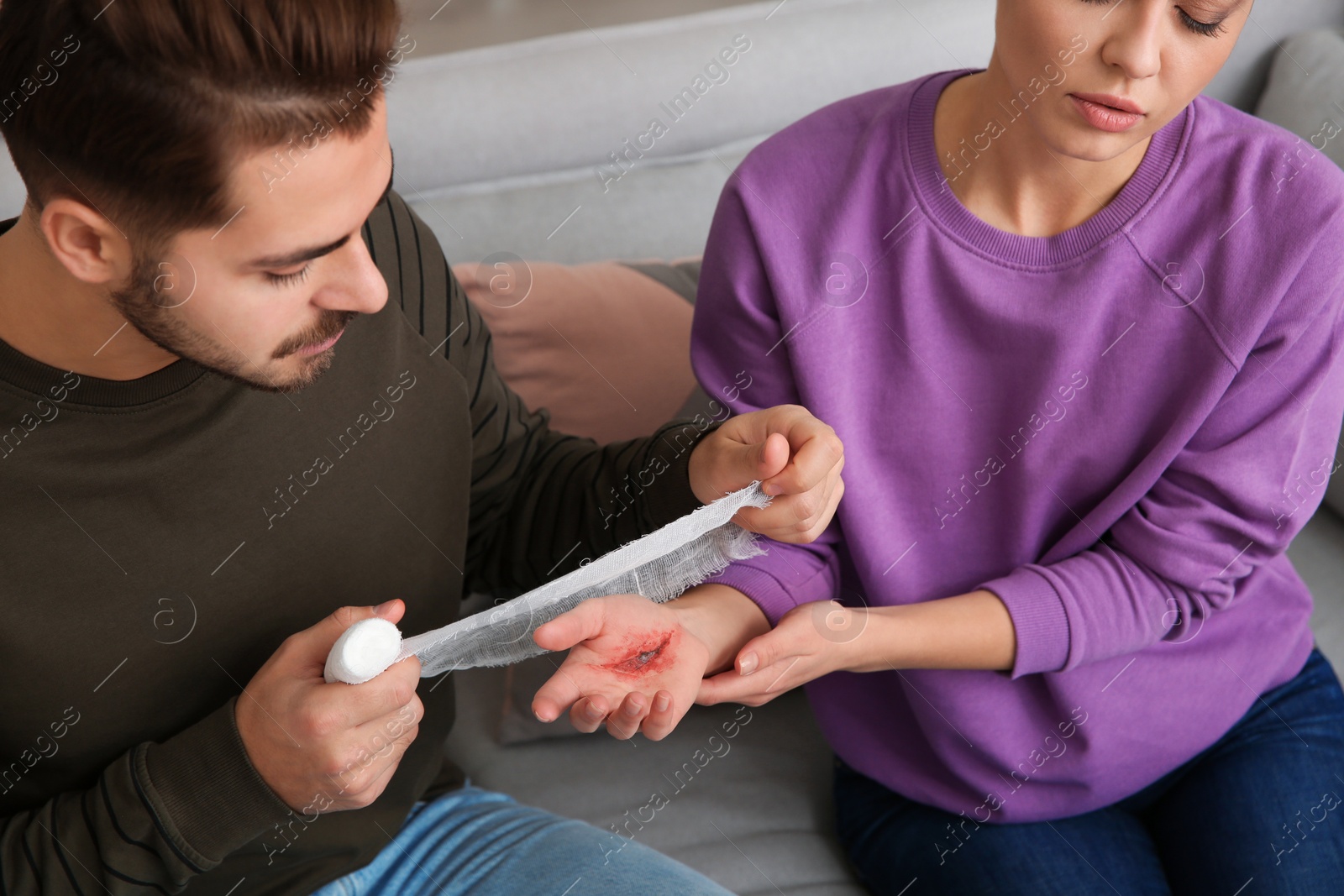 Photo of Young man applying bandage on woman's injured hand at home, closeup. First aid