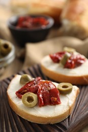 Photo of Delicious bruschettas with ricotta cheese, sun dried tomatoes and olives on table, closeup