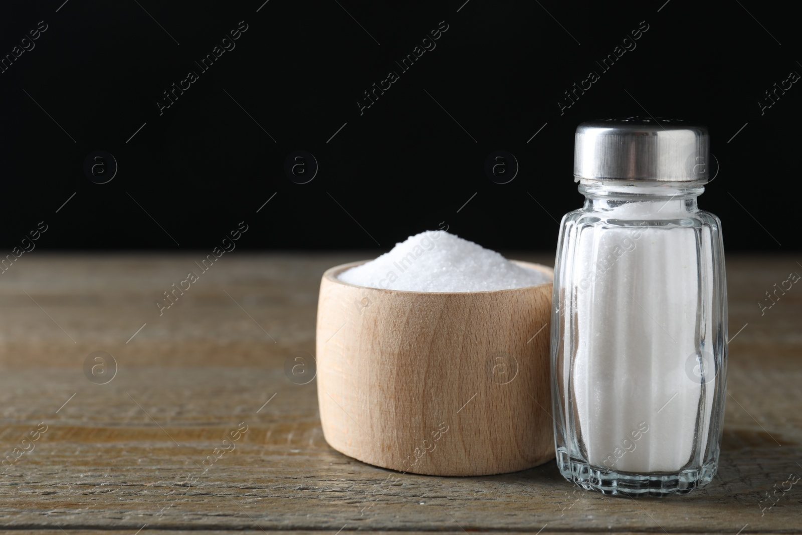 Photo of Organic salt in bowl and glass shaker on wooden table, closeup. Space for text