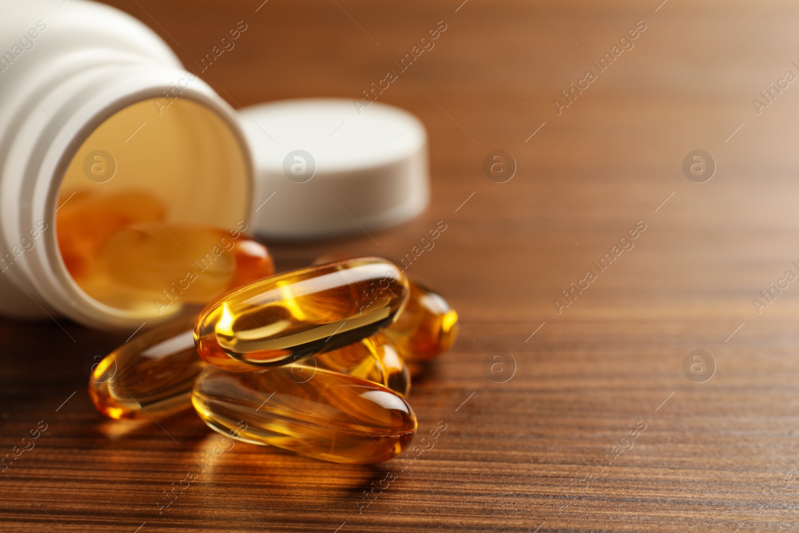 Photo of Overturned bottle with dietary supplement capsules on wooden table, closeup. Space for text