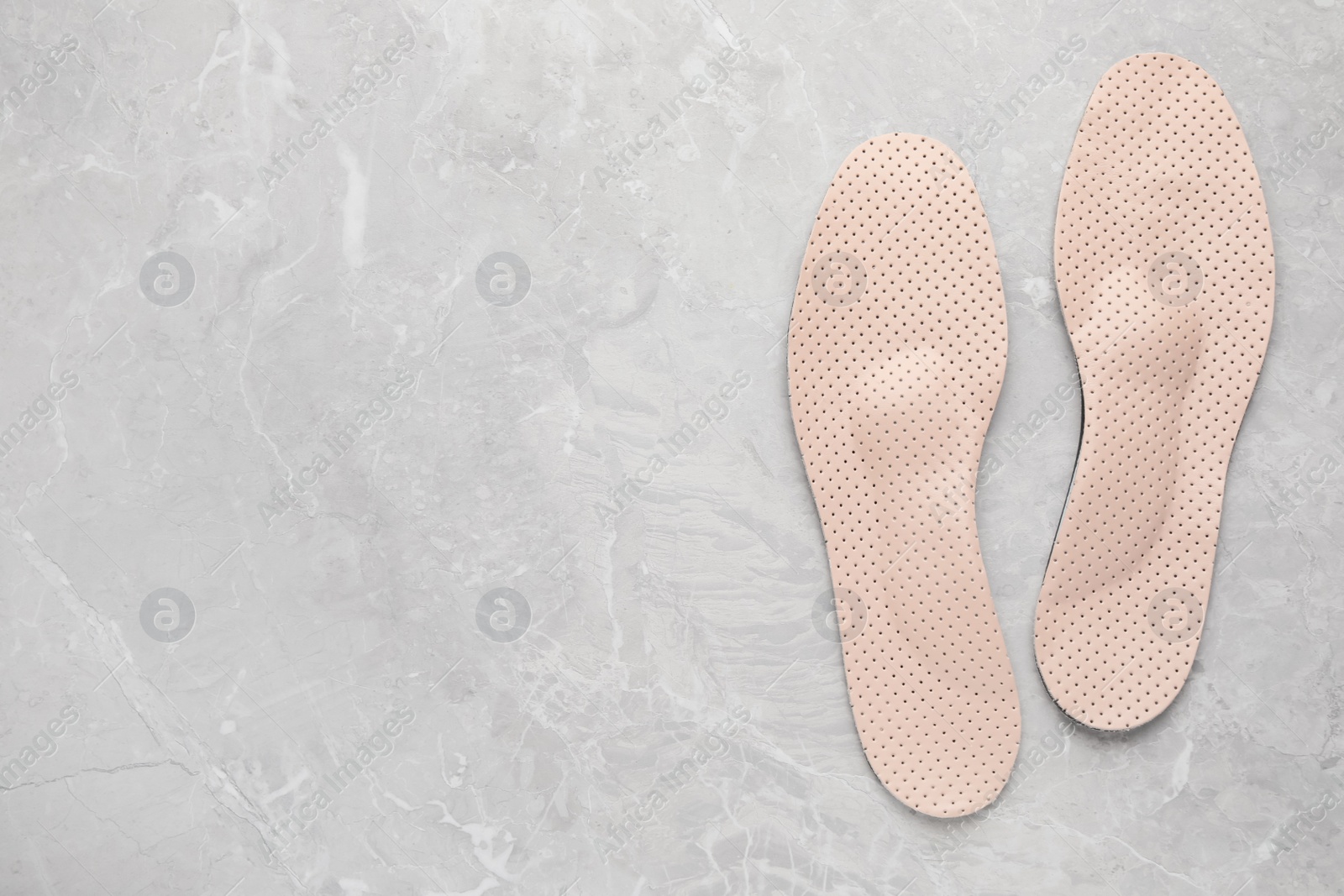 Photo of Beige orthopedic insoles on light grey marble background, flat lay. Space for text