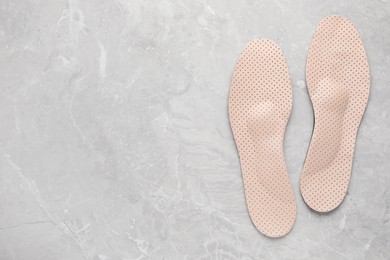 Photo of Beige orthopedic insoles on light grey marble background, flat lay. Space for text