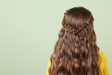 Photo of Little girl with braided hair on light green background, back view. Space for text
