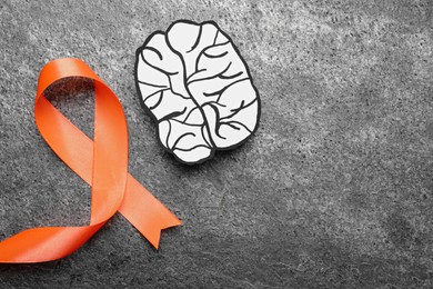 Photo of Orange ribbon and paper brain cutout on grey table, flat lay with space for text. Multiple sclerosis awareness