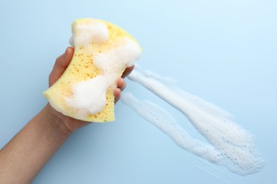 Photo of Man holding sponge with foam on light blue background, top view