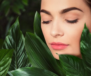 Image of Beautiful young woman feeling harmony while enjoying nature. Girl surrounded by green leaves, closeup