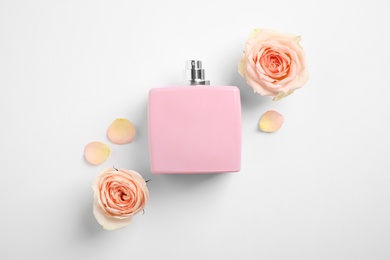 Photo of Bottle of perfume, beautiful roses and petals on white background, flat lay