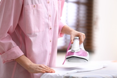 Woman ironing shirt on board indoors, closeup