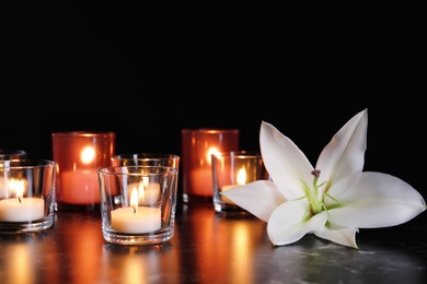 White lily and burning candles on table in darkness. Funeral symbol