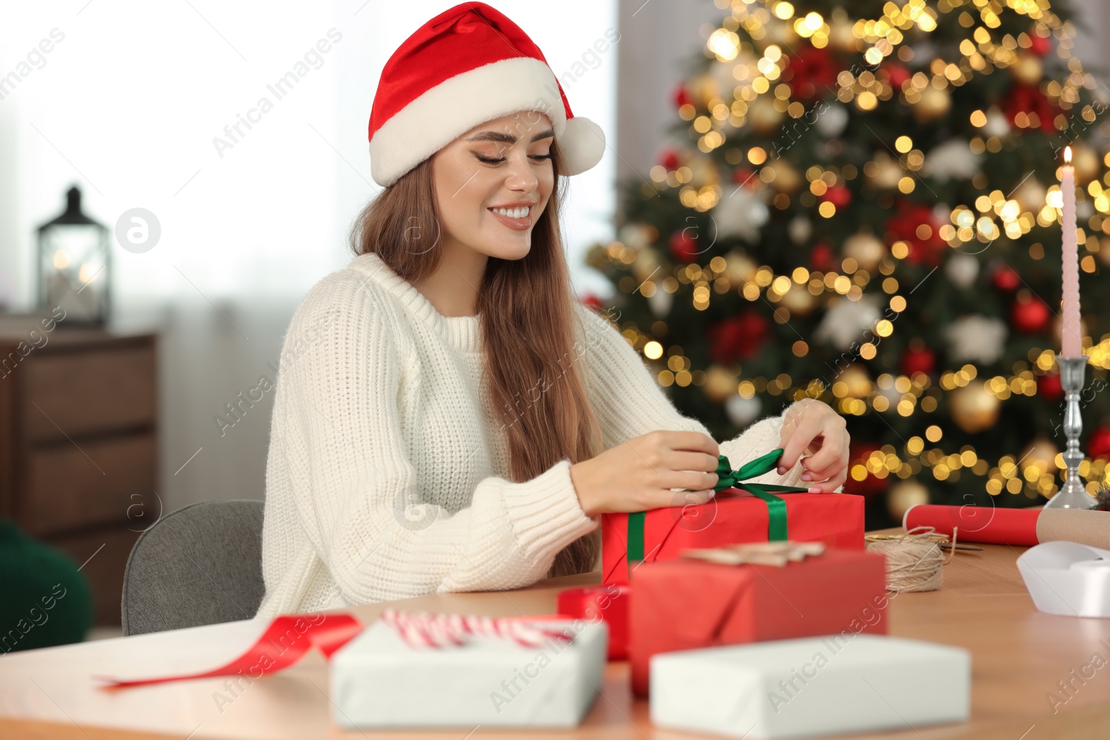 Photo of Beautiful young woman decorating Christmas gift at table in room