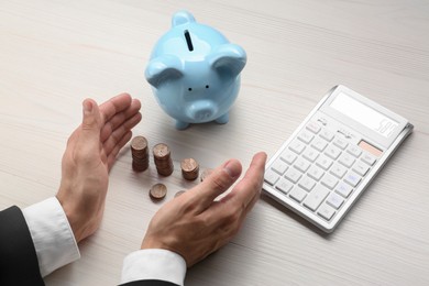 Photo of Budget planning. Businessman with coins, piggy bank and calculator at light wooden table, closeup