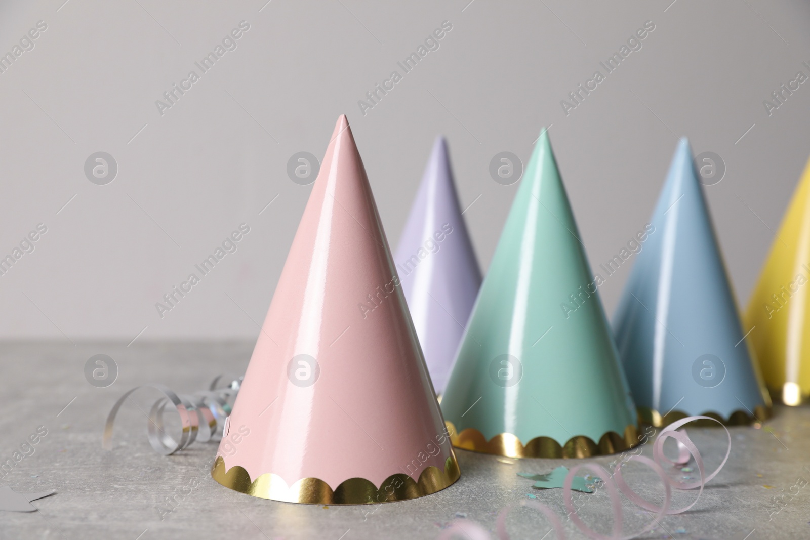 Photo of Birthday party hats, serpentine streamers and confetti on grey table
