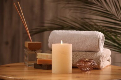 Photo of Spa composition. Burning candles, towels, soap and reed air freshener on wooden table, closeup