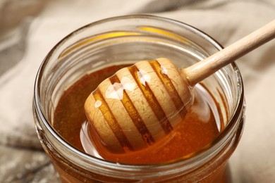 Pouring honey from dipper into jar on table, closeup