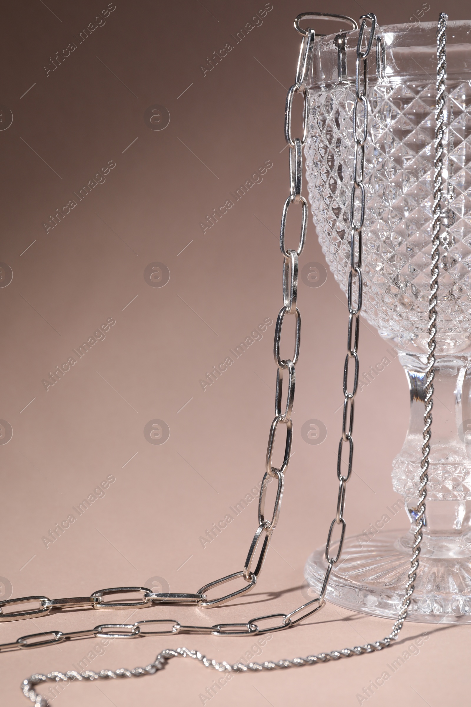 Photo of Different metal chains and glass on light brown background, space for text. Luxury jewelry