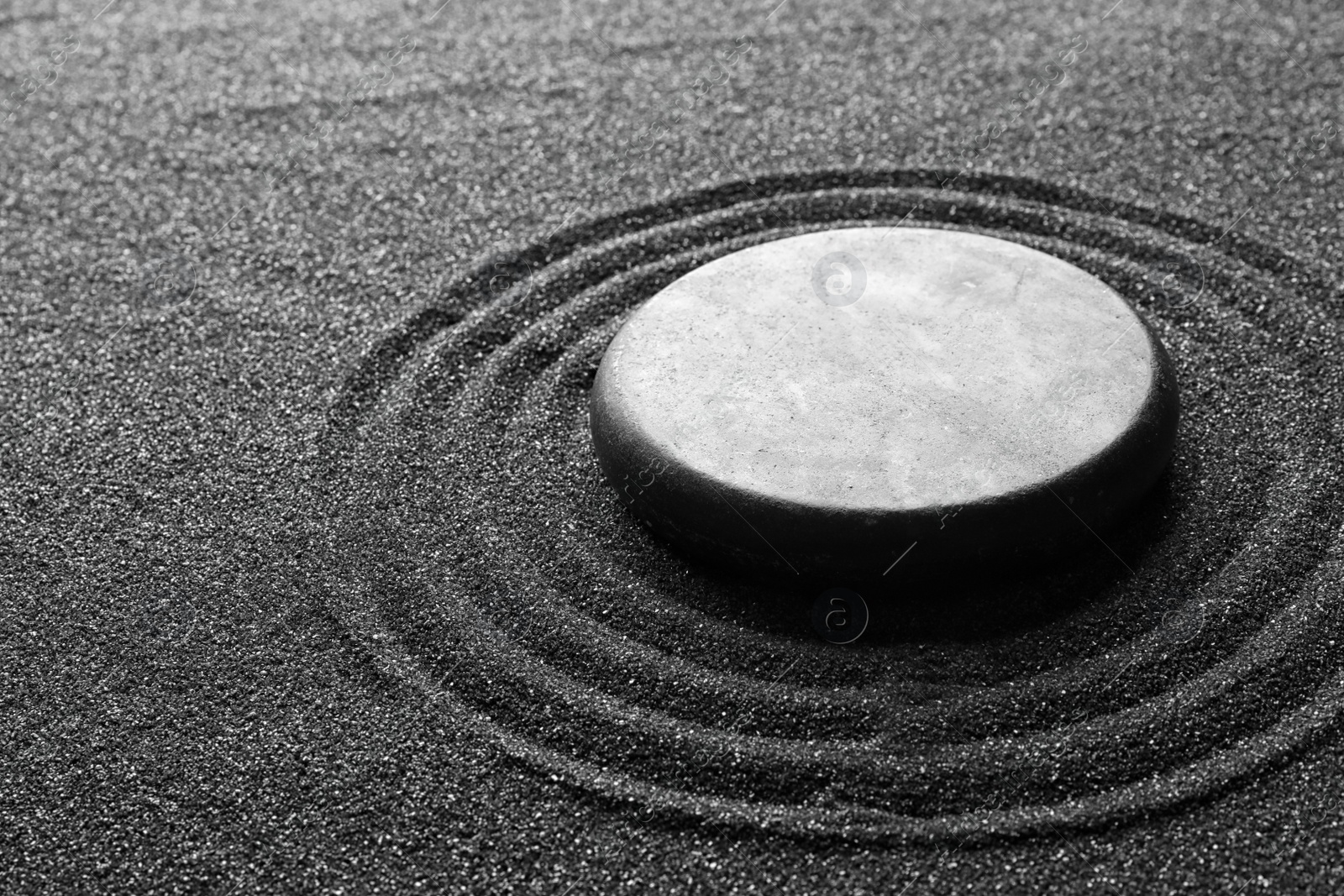 Photo of Zen garden stone on black sand with pattern, closeup