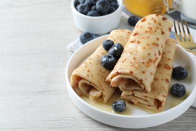 Photo of Delicious crepes with blueberries and honey on white wooden table. Space for text