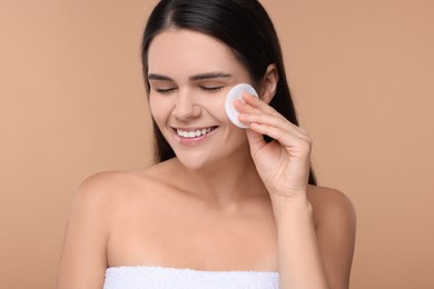 Photo of Young woman cleaning her face with cotton pad on beige background