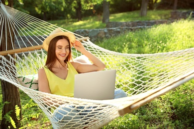 Photo of Young woman with laptop resting in comfortable hammock at green garden
