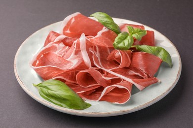 Photo of Slices of tasty cured ham and basil on grey background, closeup