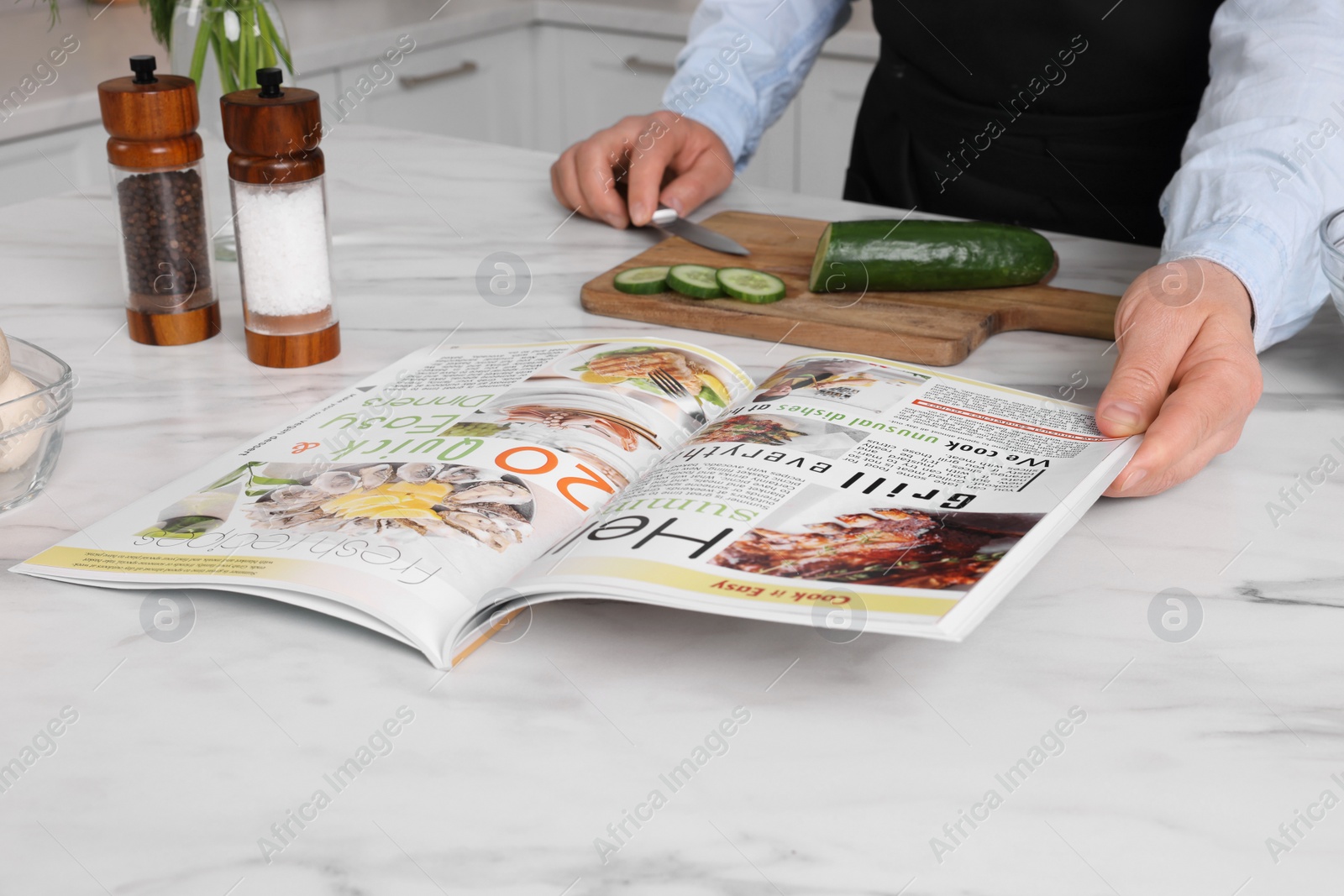 Photo of Man reading recipe in culinary magazine while cooking at home, closeup