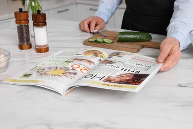 Photo of Man reading recipe in culinary magazine while cooking at home, closeup