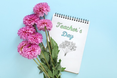 Photo of Beautiful flowers and notebook with words TEACHER'S DAY on light blue background, flat lay