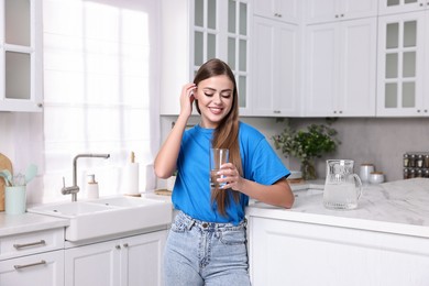 Photo of Happy woman with glass of fresh water in kitchen