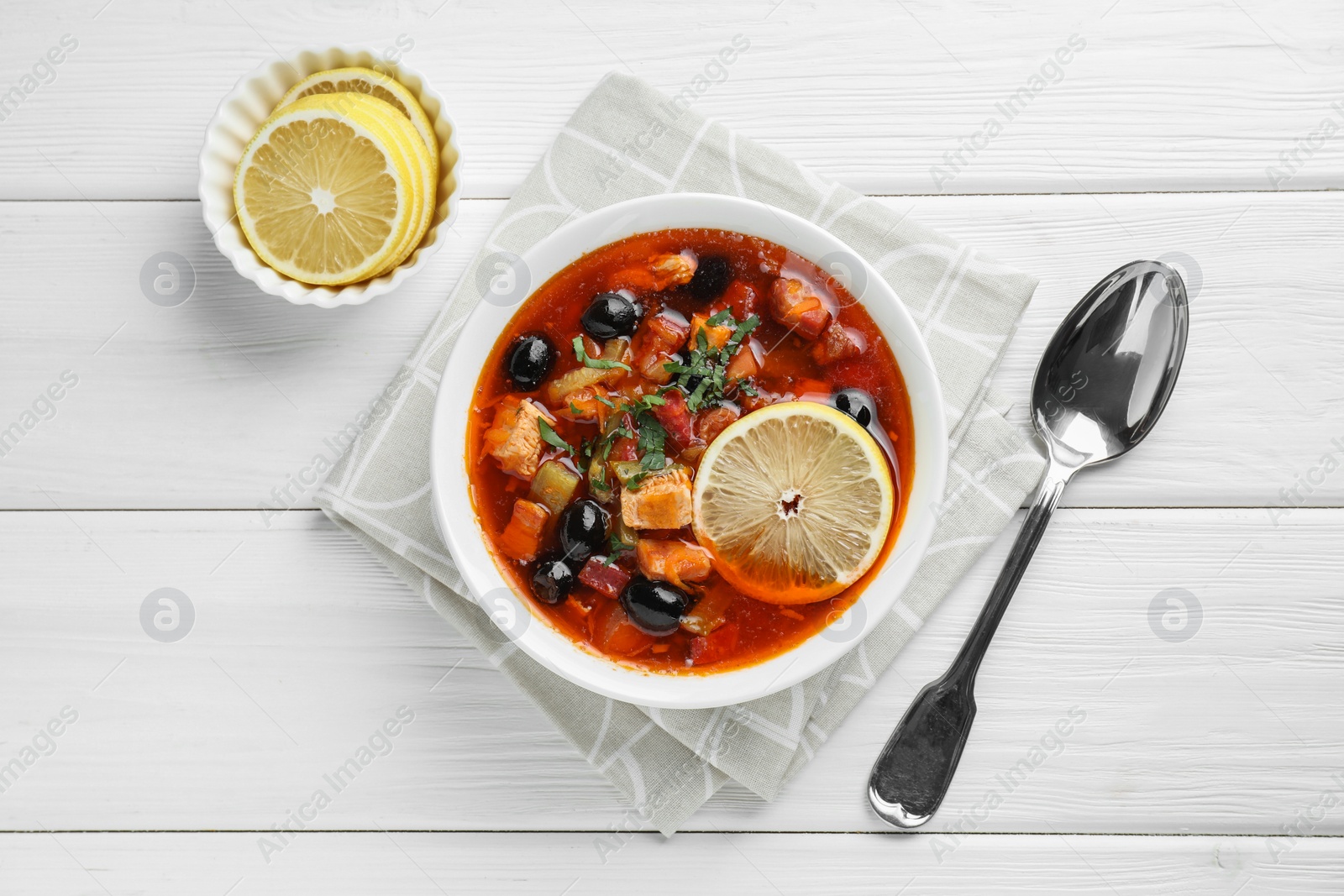 Photo of Meat solyanka soup with sausages, olives and vegetables served on white wooden table, flat lay