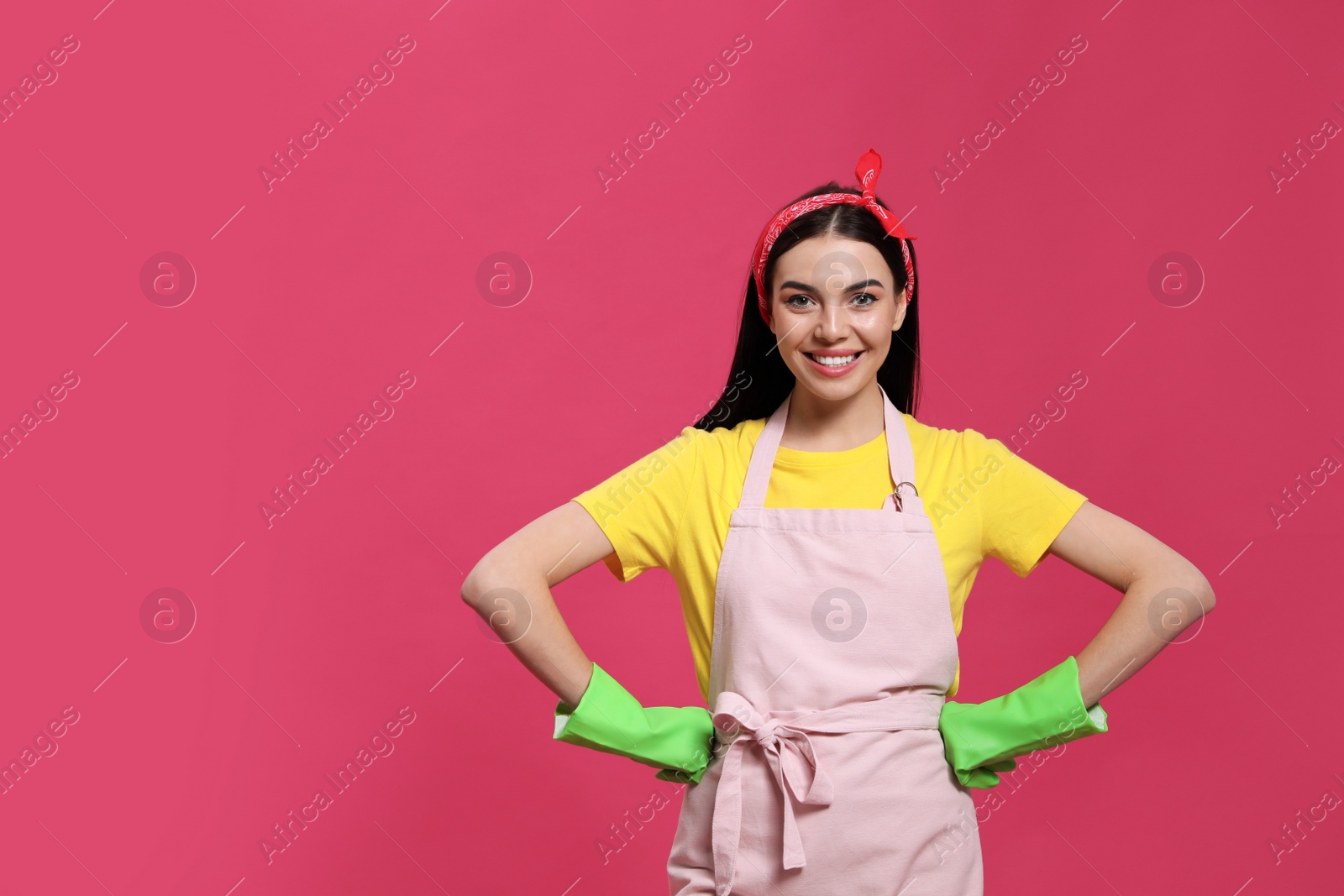 Photo of Young housewife wearing rubber gloves on pink background, space for text