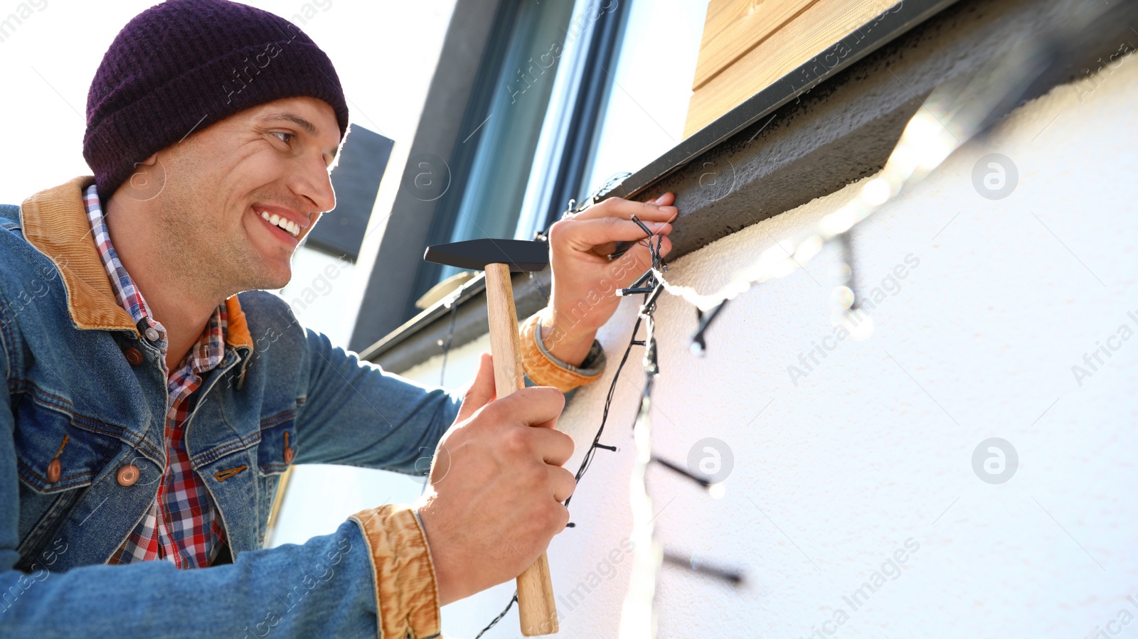 Photo of Man decorating house with Christmas lights outdoors