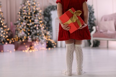 Photo of Cute little child hiding Christmas gift behind her back at home. Space for text