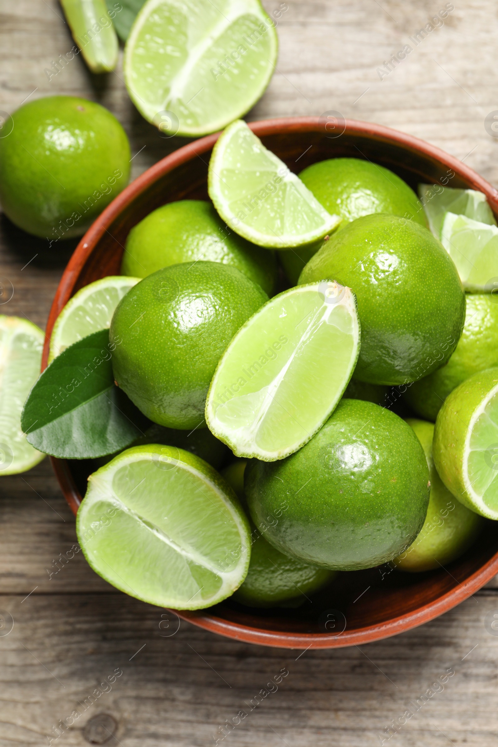 Photo of Tasty ripe limes in bowl on wooden table, top view