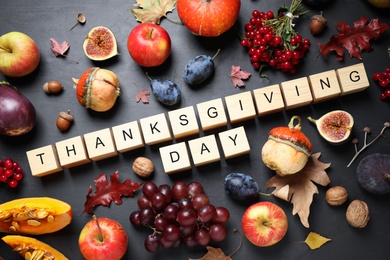 Photo of Cubes with phrase THANKSGIVING DAY, autumn fruits and vegetables on dark background, flat lay. Happy holiday