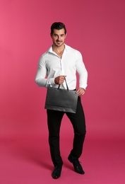 Young handsome man holding black paper bag on pink background. Mockup for design