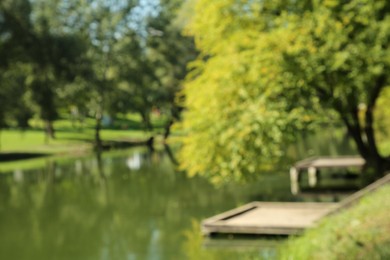 Photo of Blurred view of quiet park with green trees and pond on sunny day