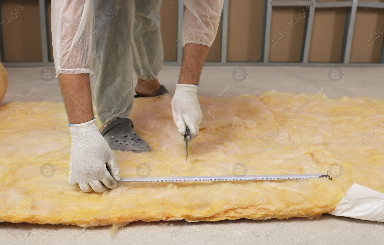 Photo of Worker measuring and cutting insulation material indoors, closeup. Space for text