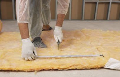 Photo of Worker measuring and cutting insulation material indoors, closeup. Space for text