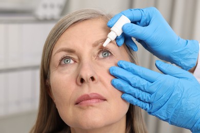 Medical drops. Doctor dripping medication into woman's eye indoors