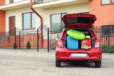 Photo of Suitcases, toys and hat in car trunk on city street. Space for text