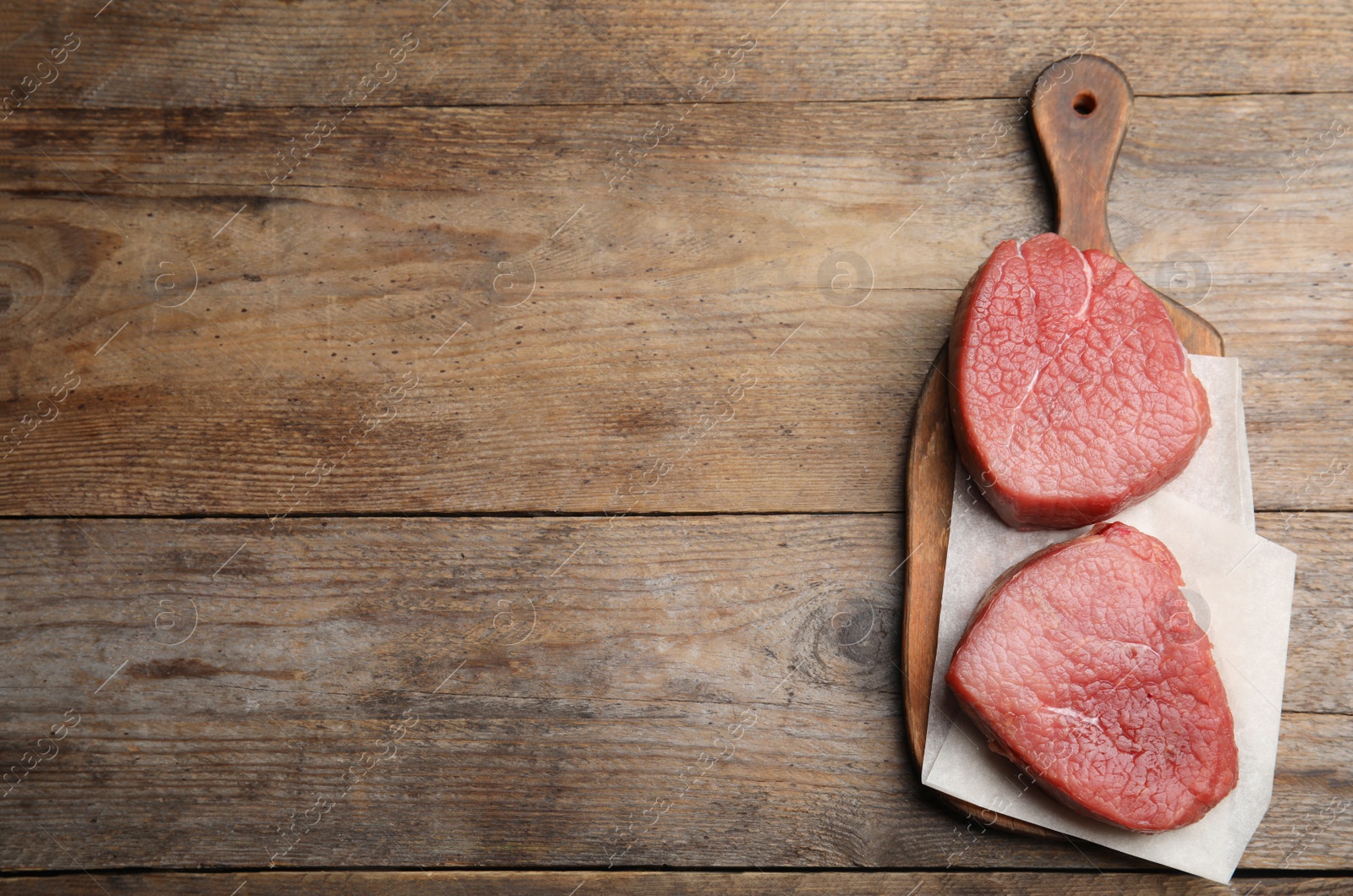 Photo of Fresh raw beef cut on wooden table, top view. Space for text