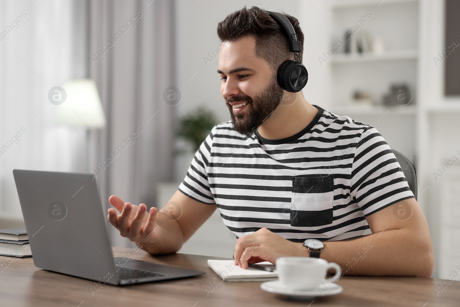 Photo of Young man in headphones using video chat during webinar at table in room