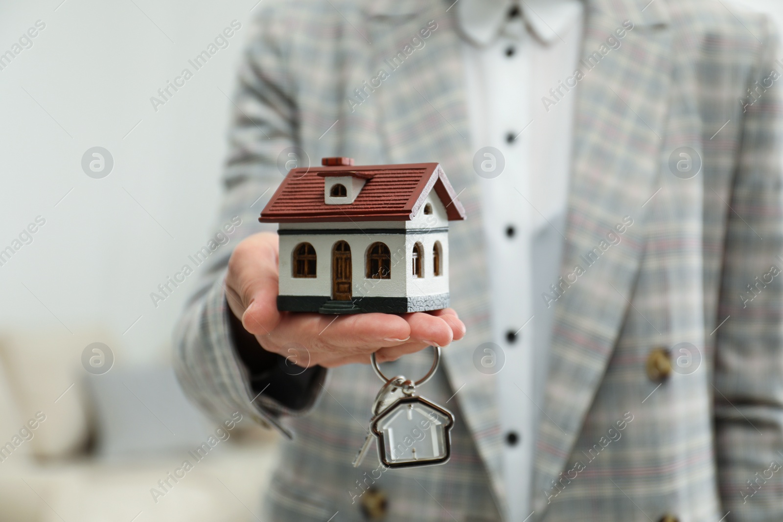 Photo of Real estate agent holding house model and key indoors, closeup