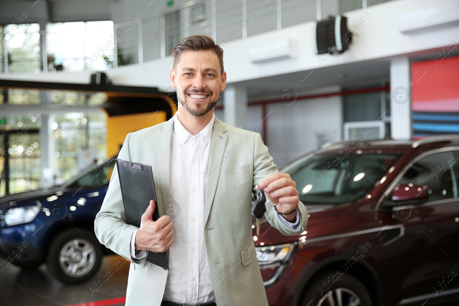 Photo of Salesman with clipboard and car keys in modern auto dealership