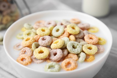 Photo of Tasty colorful cereal rings and milk in bowl on table, closeup