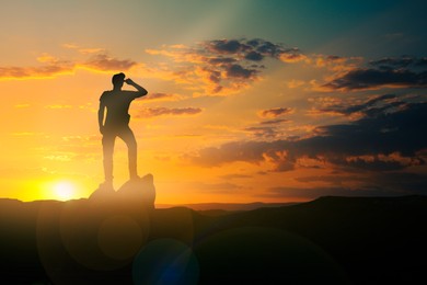 Image of Silhouette of man standing on cliff in mountains under beautiful sky at sunset. Space for text