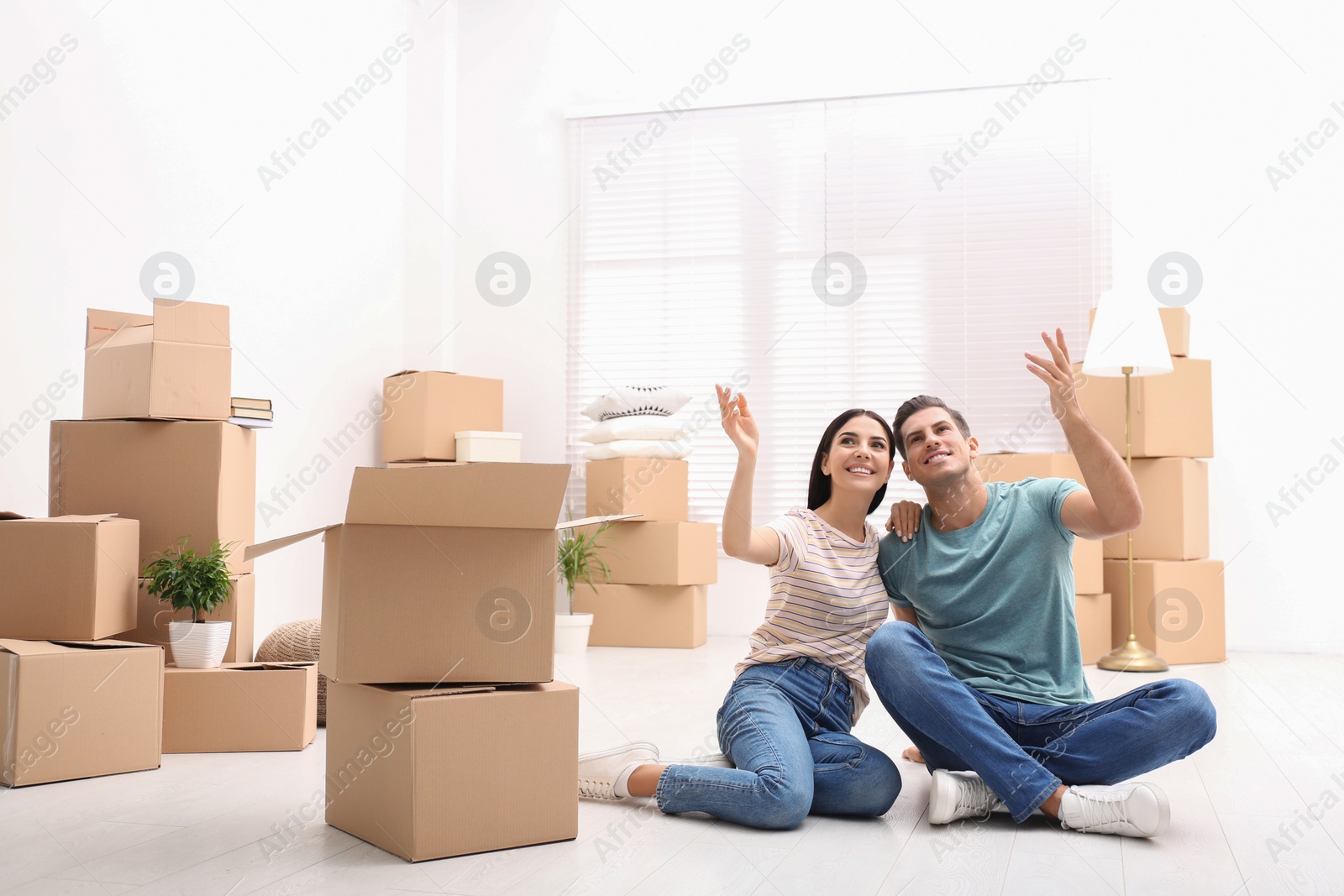 Photo of Happy couple in room with cardboard boxes on moving day